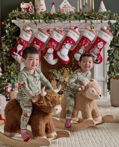 two children sitting on a rocking horse with christmas stockings hanging over the fire place behind them