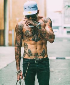 a shirtless man with tattoos on his chest talking on a cell phone while holding a bag