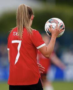 a woman holding a soccer ball in her right hand and looking at the other side