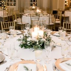 the table is set with white and gold plates, silverware, candles and greenery