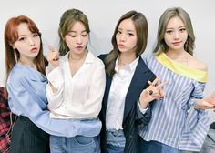 three young women standing next to each other in front of a white wall and pointing at something