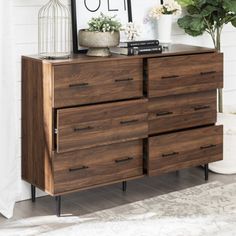 a wooden dresser sitting next to a white wall and potted plant on top of it