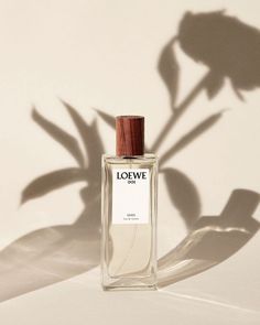 a bottle of perfume sitting on top of a white table next to a shadow of a plant