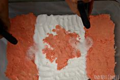 someone is spreading icing on a cake with orange and white frosting in a pan