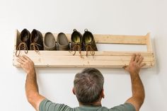 a man holding up a wooden shelf with shoes on it and hanging from the wall