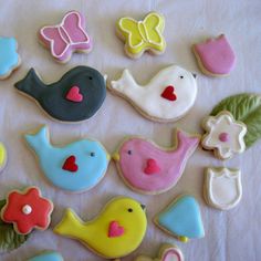 decorated cookies arranged in different shapes and colors on a white tablecloth with butterfly, bird, flower, and leaf decorations