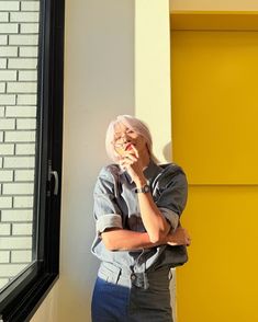 an older woman standing in front of a yellow wall with her arms crossed and looking at the camera