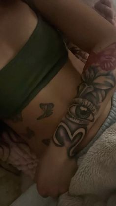 a woman laying on top of a bed with tattoos on her stomach and arm behind her back