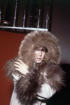 a woman wearing a fur hat and coat in front of a red wall at night