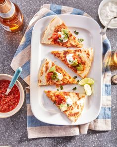 four slices of pizza on a white plate with salsa and sour cream in the background