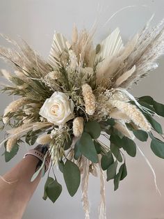 a person holding a bouquet with white flowers and greenery on the top of it