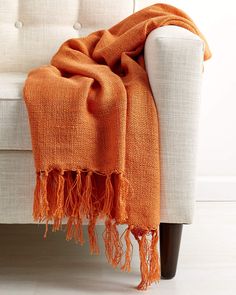 an orange blanket is draped over a white couch with a black leg and wooden legs