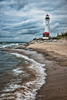 a light house sitting on top of a sandy beach next to the ocean with waves coming in