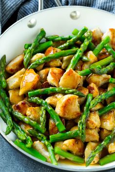 a white bowl filled with chicken and asparagus on top of a blue table