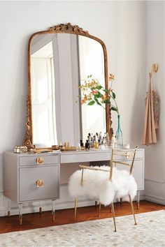 a dressing table with a mirror, stool and rug in a white room next to a window