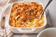 a casserole dish with meat and potatoes in it on a table next to two silver spoons