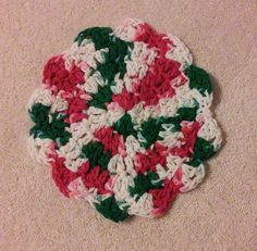 a crocheted dishcloth with red, white and green flowers on it sitting on the floor