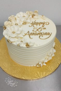 a white and gold wedding cake with flowers on the top is sitting on a golden plate