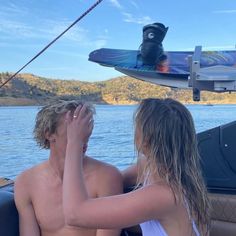 two people sitting on a boat looking at something in the air above their head, with a surfboard behind them