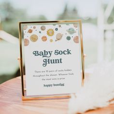 a baby sock hunt sign sitting on top of a wooden table next to a white feather