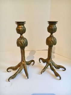 two metal candlesticks sitting on top of a white table next to each other