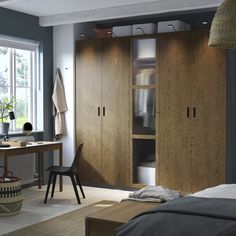 a bedroom with a bed, desk and cupboards in the corner next to a window