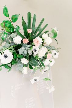 a vase filled with flowers and greenery on top of a white table cloth covered wall