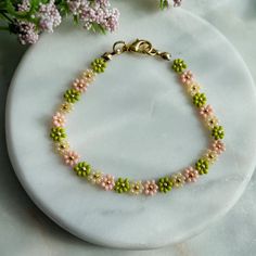 a pink and green beaded bracelet on a white marble surface with flowers in the background