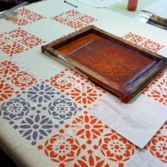 an orange and white table cloth with decorative designs on it, next to a wooden tray