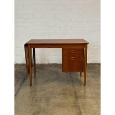 a wooden desk with two drawers in front of a white brick wall and concrete floor