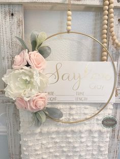 a white sign with flowers hanging from it's side next to a wooden frame