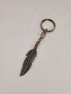 a metal keychain with a feather on it sitting on a white counter top