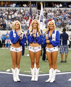 two cheerleaders standing on the sidelines at a football game, one holding a microphone