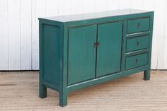 a green cabinet sitting on top of a wooden floor next to a white painted wall