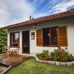 a small white house with wooden shutters on the front and side windows, sitting next to a deck