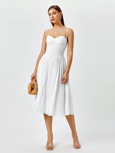 a woman is wearing a white dress and holding a handbag in her right hand