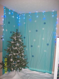 a small christmas tree in front of a blue curtain with snowflakes on it