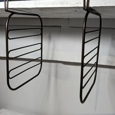 two metal racks hanging from the side of a window sill next to a white wall