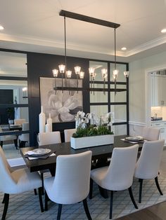 a dining room table with white chairs and lights hanging from the chandelier above it