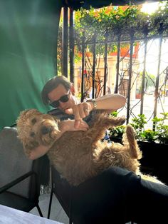 a man sitting on top of a chair holding a brown dog in his lap and petting it