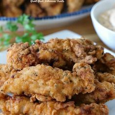 some fried food on a white plate next to a bowl of ranch dressing and dipping sauce