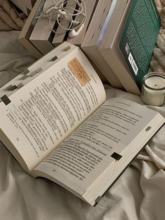 an open book sitting on top of a bed next to a candle and some books