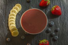 a smoothie with bananas, strawberries and blueberries on a slate table top