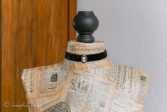 a mannequin made out of old newspaper with a black leather neck tie and button