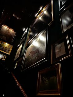 many framed pictures hang on the wall in a dark room with stairs leading up to them