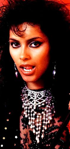 a close up of a person with long hair and jewelry on her neck, posing for the camera