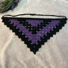 a crocheted triangle is laying on a white surface next to some purple flowers