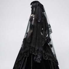 a woman wearing a black veil and dress with flowers on the skirt is standing in front of a gray sky