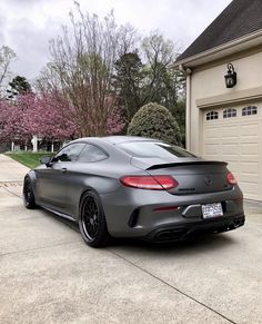 a grey mercedes benz coupe parked in front of a house with pink flowers on the driveway