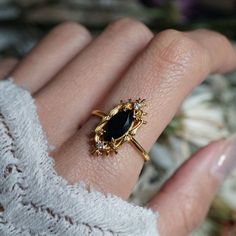 a woman's hand wearing a gold ring with an oval black stone on it